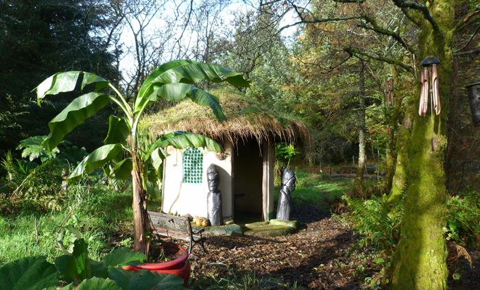 Jungle hut with turf roof and large African style carvings. Banana tree in the foreground